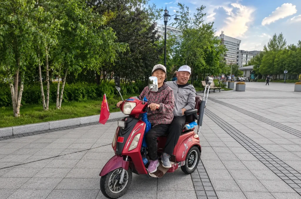 Elderly couple riding a 3 wheel electric mobility scooter in a park